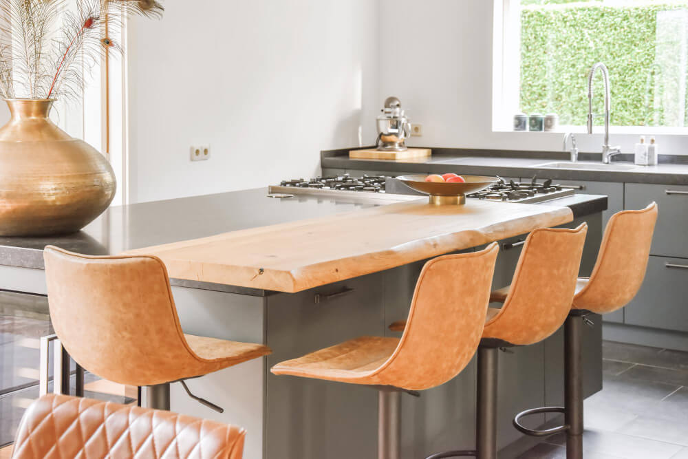 Gros plan sur le débord d'un plan de travail de cuisine (îlot central), avec des tabourets en dessous.