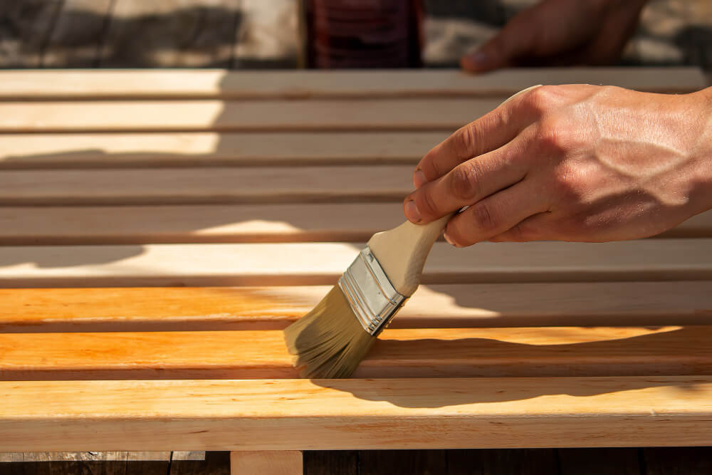 Huile de décoffrage : quelles sont les alternatives écologiques ou maison ? 11 Personne appliquant de l'huile de colza avec un pinceau sur un coffrage en bois.