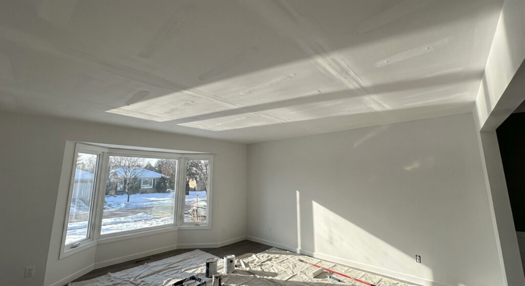 Plafond fraîchement peint révélant les "fantômes" des bandes à joint sous la lumière d'une baie vitrée, défaut esthétique majeur en finition intérieure