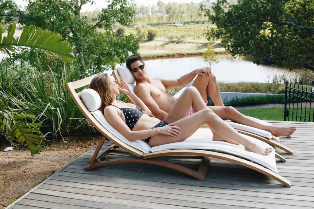 Comment aménager un espace détente autour d’un transat ? 2 Deux transats modernes en bois installés au bord d'une piscine avec des coussins confortables pour un espace détente réussi.
