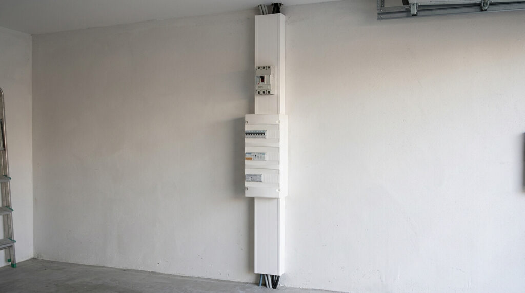: Une gaine technique de logement en PVC blanc installée au mur avec le tableau électrique et le disjoncteur général fixés dessus.