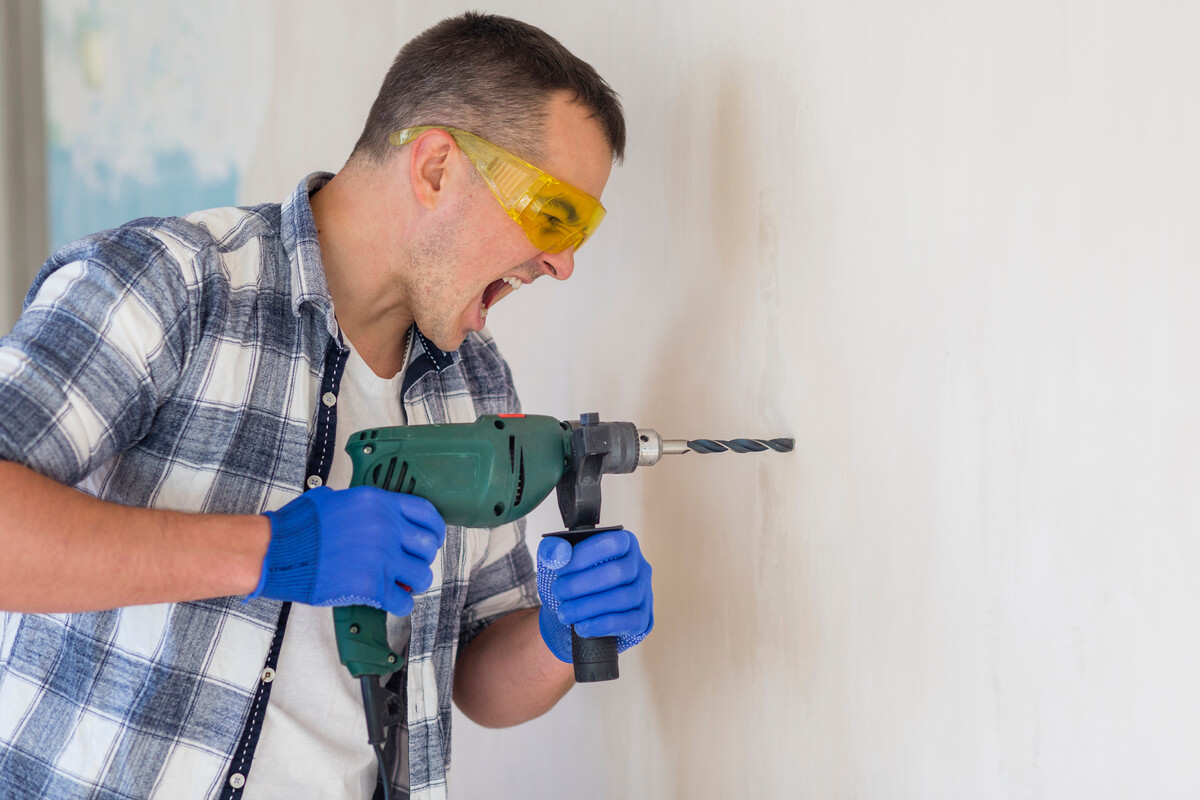 Un bricoleur perçant un mur blanc en carreaux de plâtre à l'aide d'une perceuse sans fil.