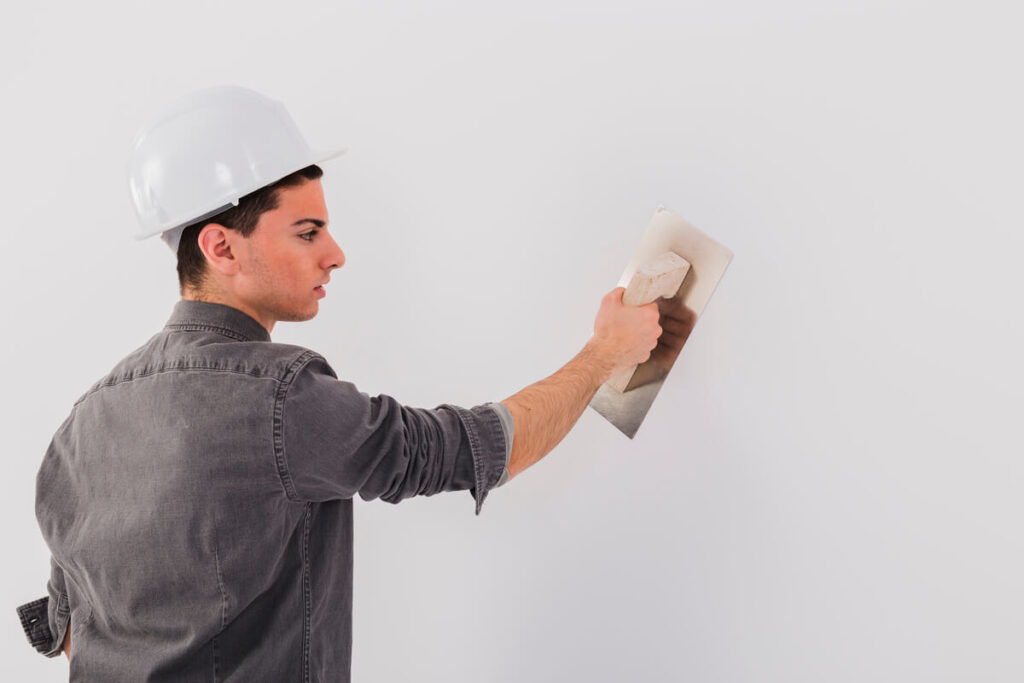 Peinture qui s'écaille en passant le rouleau : causes et solutions pour réparer 3 Une personne appliquant un enduit de lissage sur un mur intérieur pour réparer les imperfections.