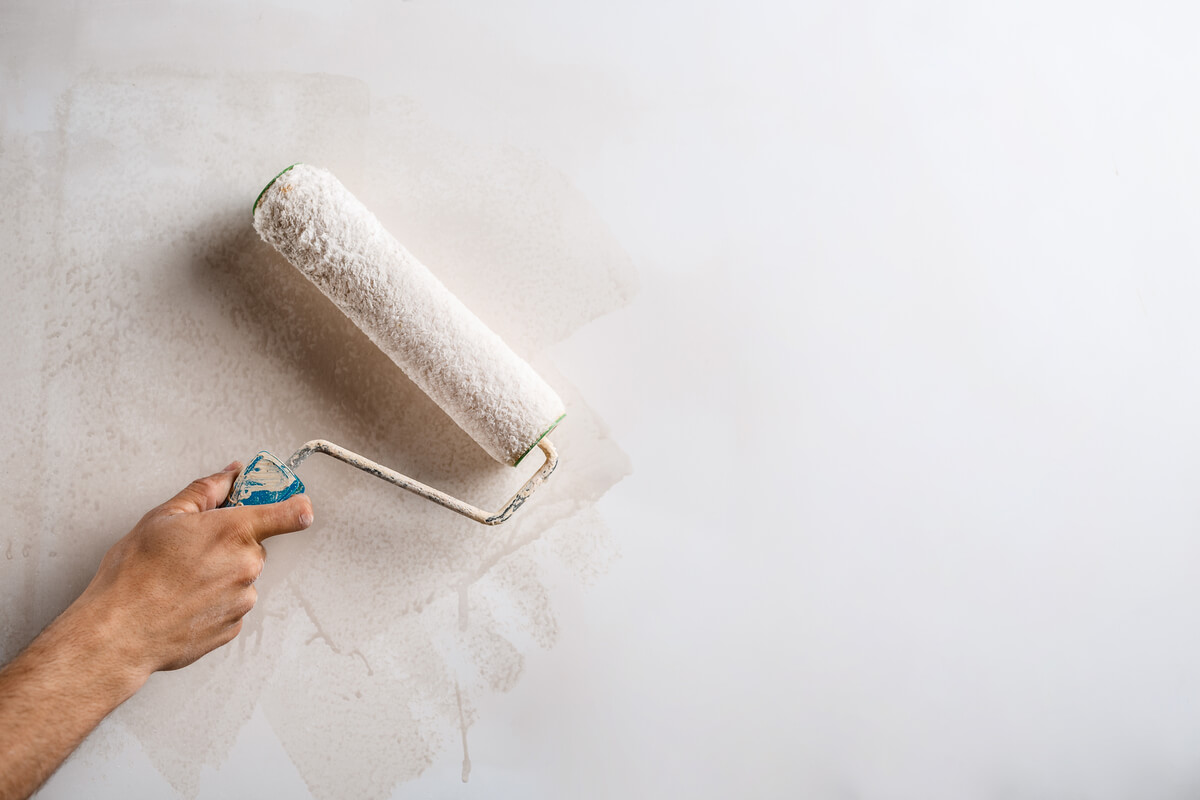 Un rouleau à peinture appliquant de la couleur blanche sur un mur où l'ancienne couche se décolle en morceaux.
