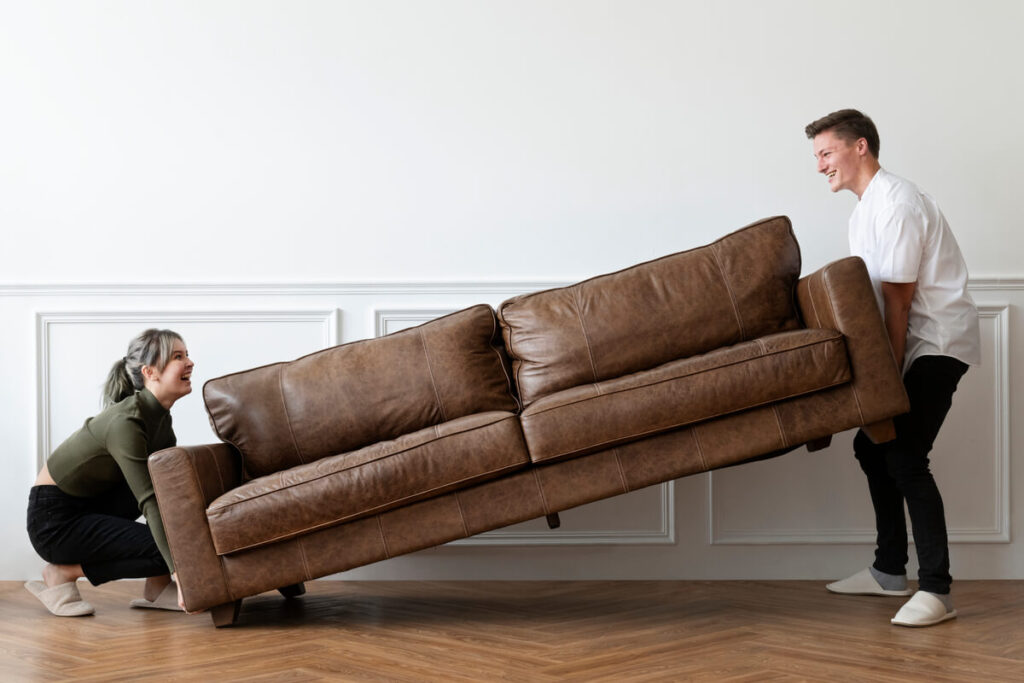 Comment faire passer un canapé plus large que la porte ? 2 Deux personnes faisant pivoter un canapé d'angle à la verticale pour franchir une porte étroite.
