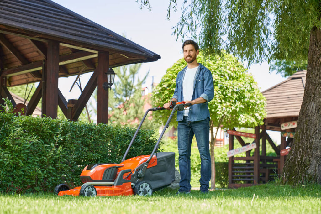 Tondeuse thermique tractée ou poussée : la pente compte autant que la surface 2 Jardinier utilisant une tondeuse thermique tractée sur une pelouse en pente inclinée.