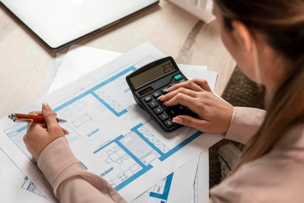 Propriétaire calculant le budget prévisionnel des travaux sur un plan de maison avec devis d'artisans.