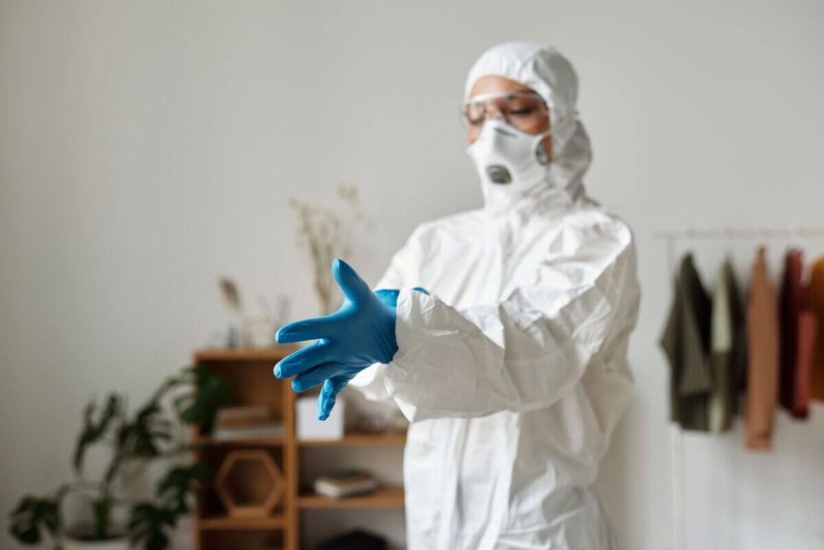 Exterminateur professionnel équipé d'un masque et d'une combinaison inspectant des traces de nuisibles dans un logement.